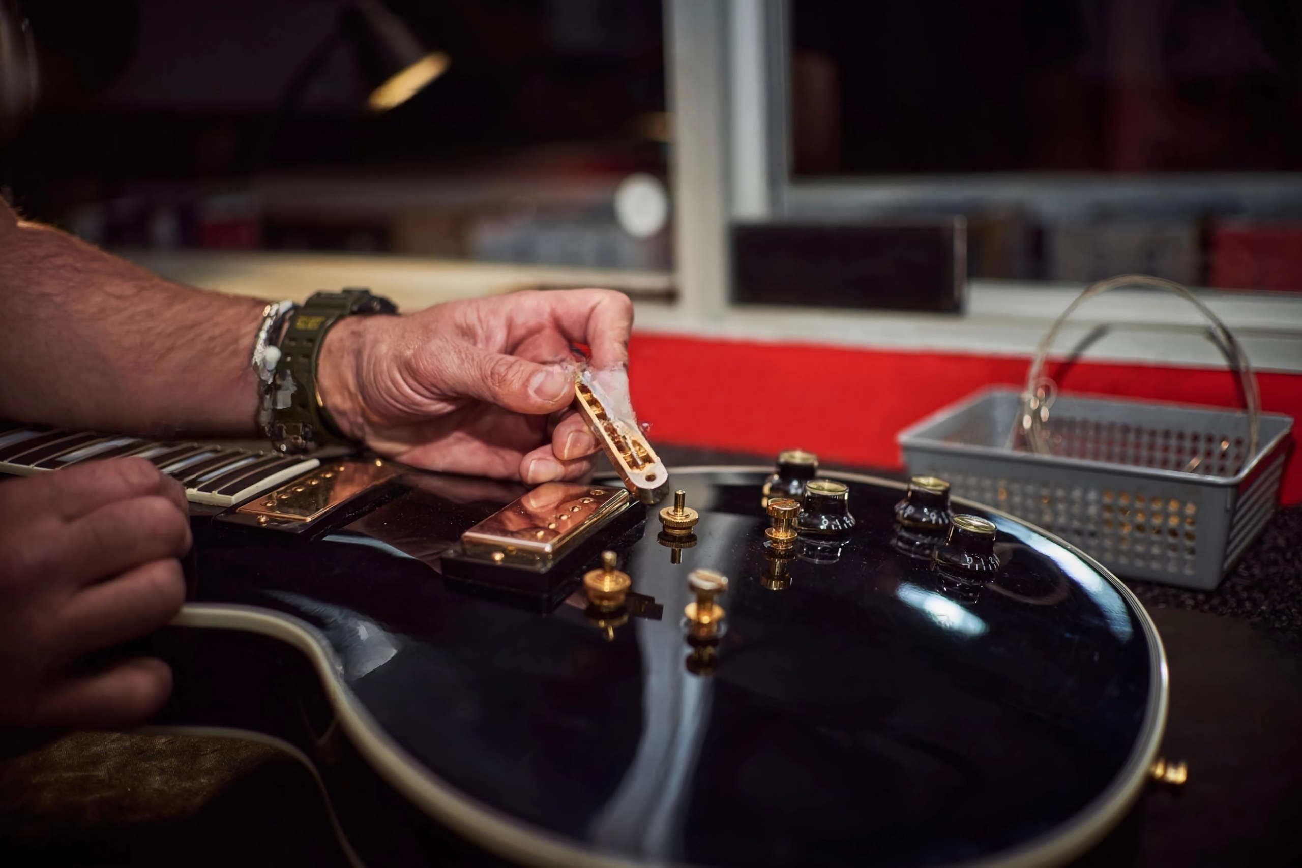 Μαύρη Les Paul με χρυσά εξαρτήματα στον πάγκο του λουθιέρη, κάτω από ζεστό φως λάμπας.