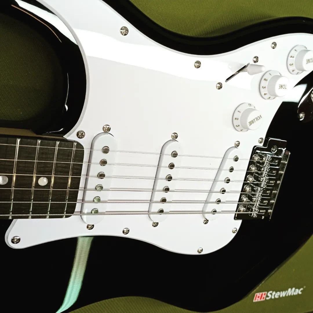 Stratocaster με μαύρο φινίρισμα, λευκό pickguard και τρία single-coil μικρόφωνα, στον πάγκο για ρύθμιση.