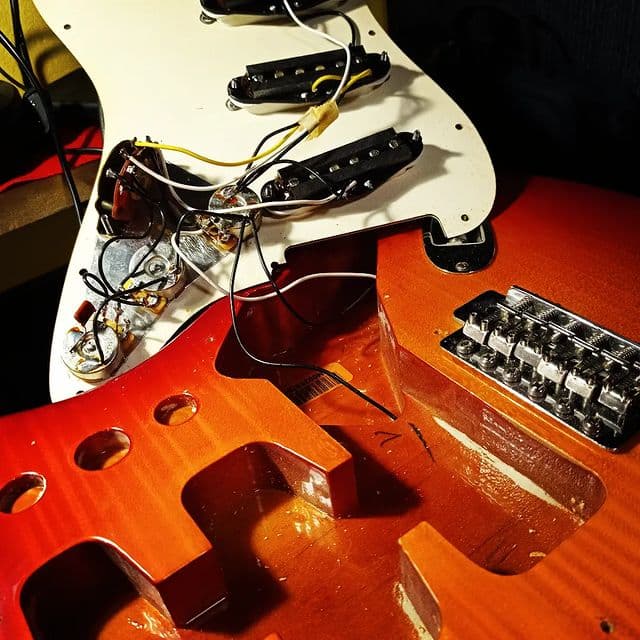 Ανοιχτή κοιλότητα σώματος sunburst Stratocaster με ορατή καλωδίωση και μικρόφωνα κατά την εργασία ηλεκτρονικών.